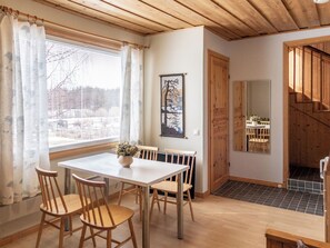 A dining area with a table and chairs, a window with curtains, a painting on the wall, and a staircase leading to another room. - Jokiniitty 2 by Interhome (Sotkamo)