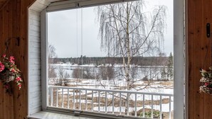 Huone, jossa on suuri ikkuna, josta avautuu näkymä lumiseen maisemaan, ja jossa on puinen sisustus sekä valkoinen kaide.