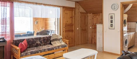 En kompakt opholdsstue med sofa, bord, stol, vaskemaskine og et ur på væggen.