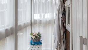 Huoneessa on puinen penkki, kukkakori ja ikkuna, jossa on ohuet verhot.