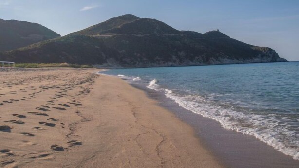 Ein Strand mit Fußspuren, die zum Wasser führen, ein Fußballtor und Berge im Hintergrund.