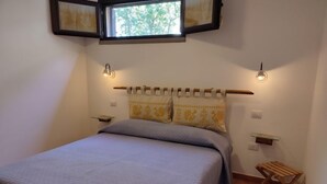 Ein Schlafzimmer mit einem Bett, zwei Nachttischen, einem Fenster und einem kleinen Holzschemel.
