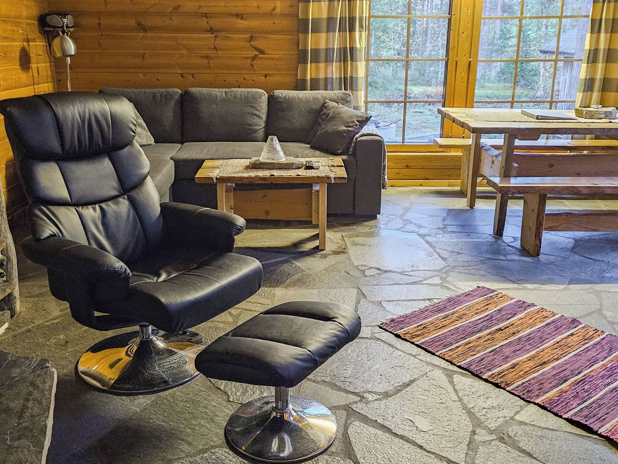 A cozy living room with a leather sofa, a black armchair, a small wooden table, and a stone floor.