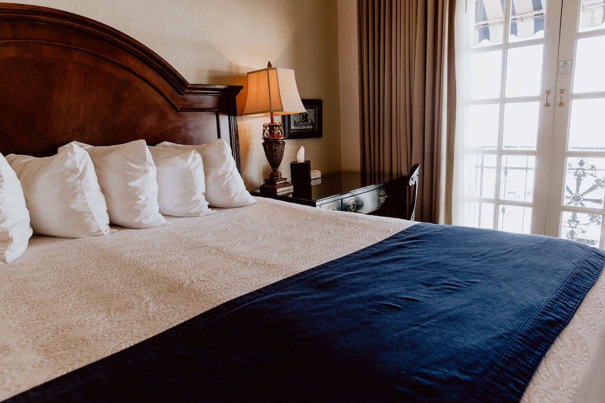 A neatly made bed with a patterned bedspread and pillows, a bedside table with a lamp, and a window with curtains.