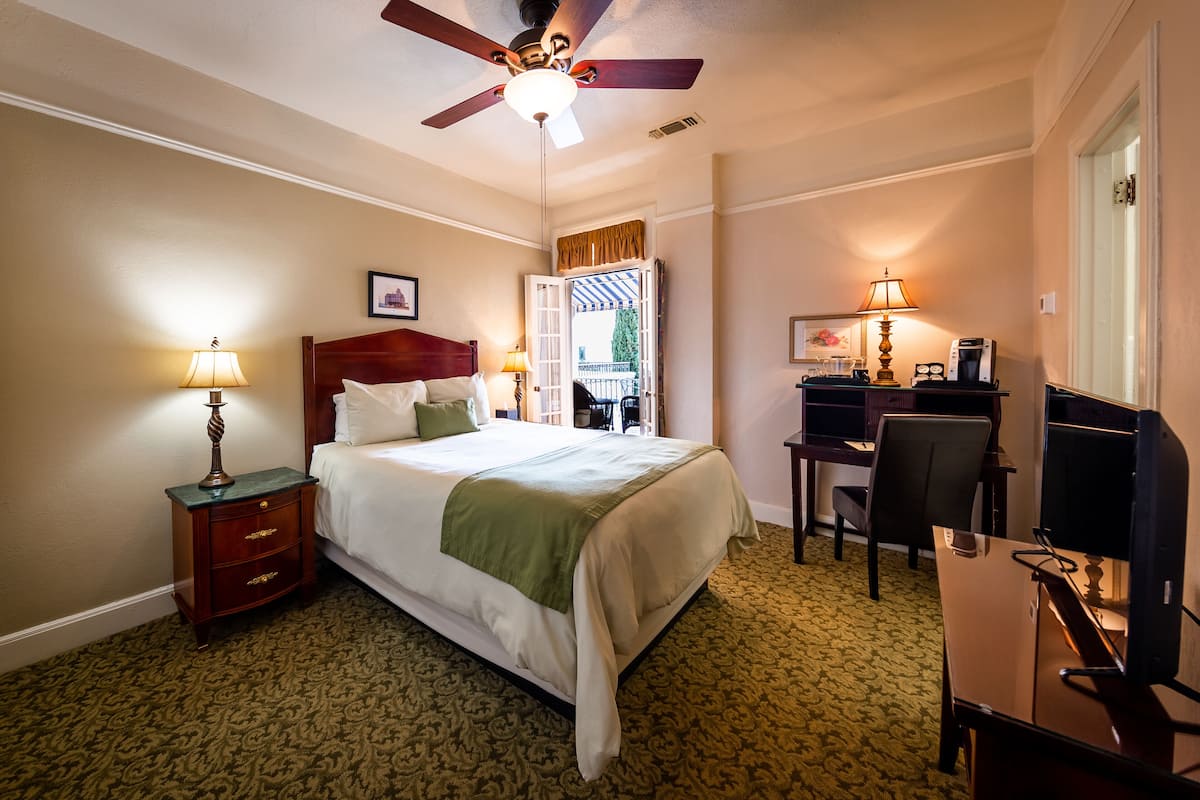 A hotel room with a bed, a desk, a chair, a television, and a ceiling fan.