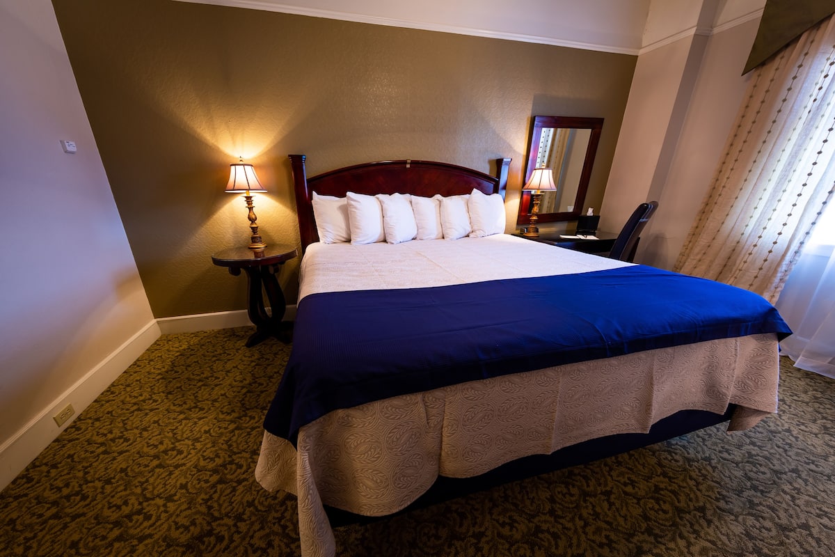 A hotel room with a large bed, two bedside lamps, a mirror, and a carpeted floor.