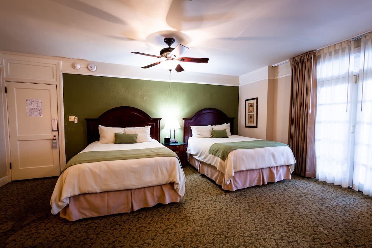 A hotel room with two beds, a ceiling fan, a carpeted floor, and a window with curtains.