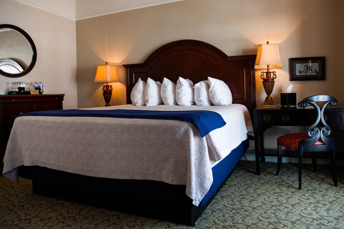 A hotel room with a large bed, two bedside lamps, a desk with a chair, a mirror, and a framed picture on the wall.