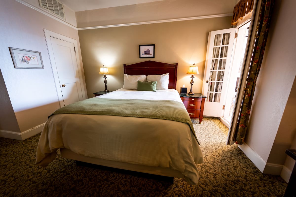 A hotel room with a large bed, two bedside lamps, a nightstand, a framed picture on the wall, and a door with a window.