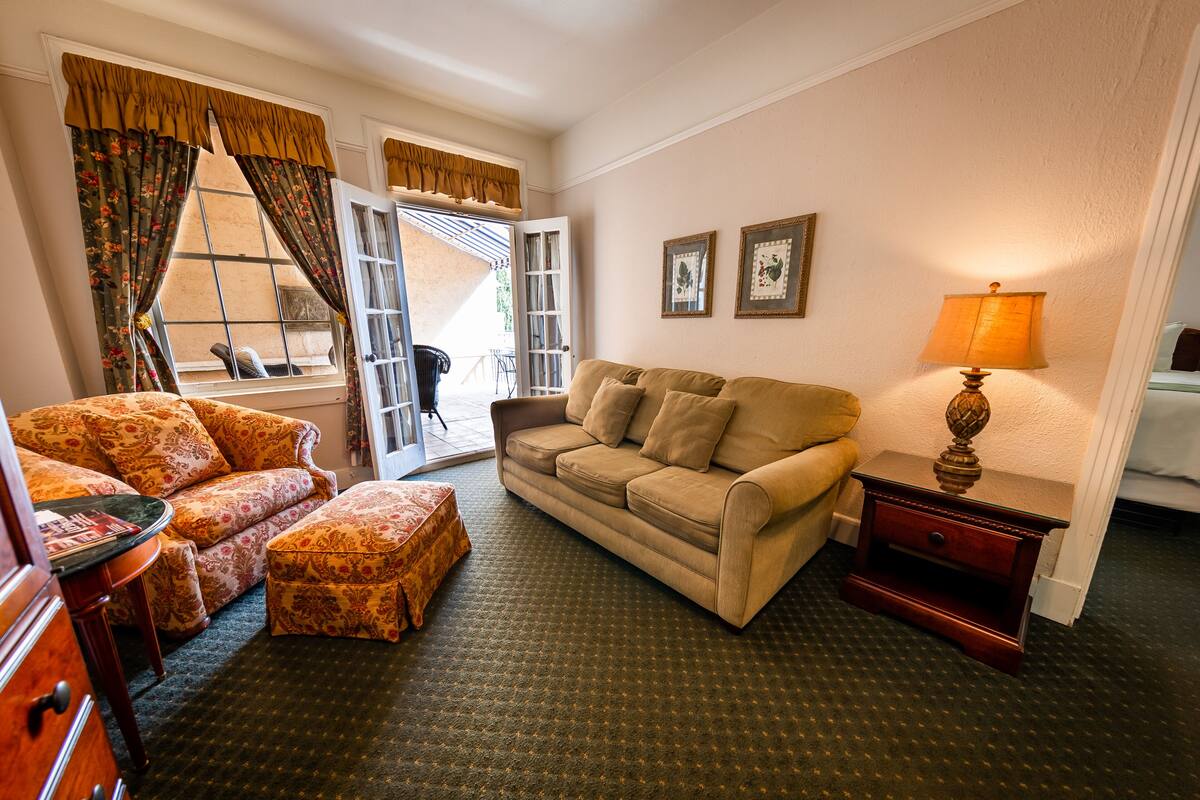 A living room with a sofa, ottoman, and a lamp. There is a window with curtains and a view outside.