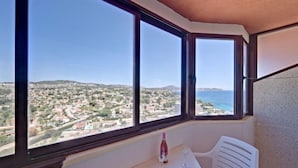 Ein Balkon mit weißem Tisch und Stuhl, einer Weinflasche und Blick auf eine Küstenstadt.