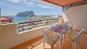 Ein Balkon mit Tisch und Stühlen, mit Blick auf eine Küstenstadt und einen markanten Berg.