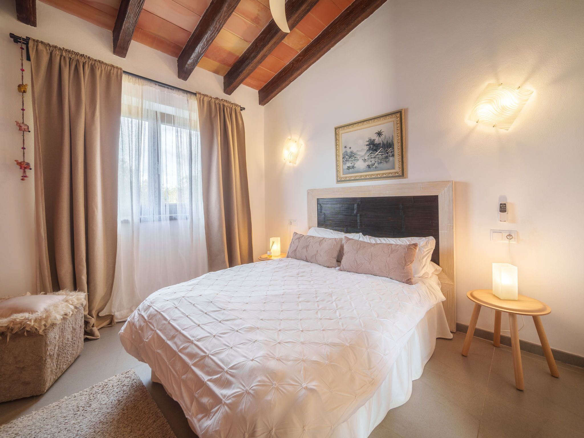 Una camera da letto con un letto grande, travi di legno a soffitto, un quadro al muro e un comodino con una lampada.