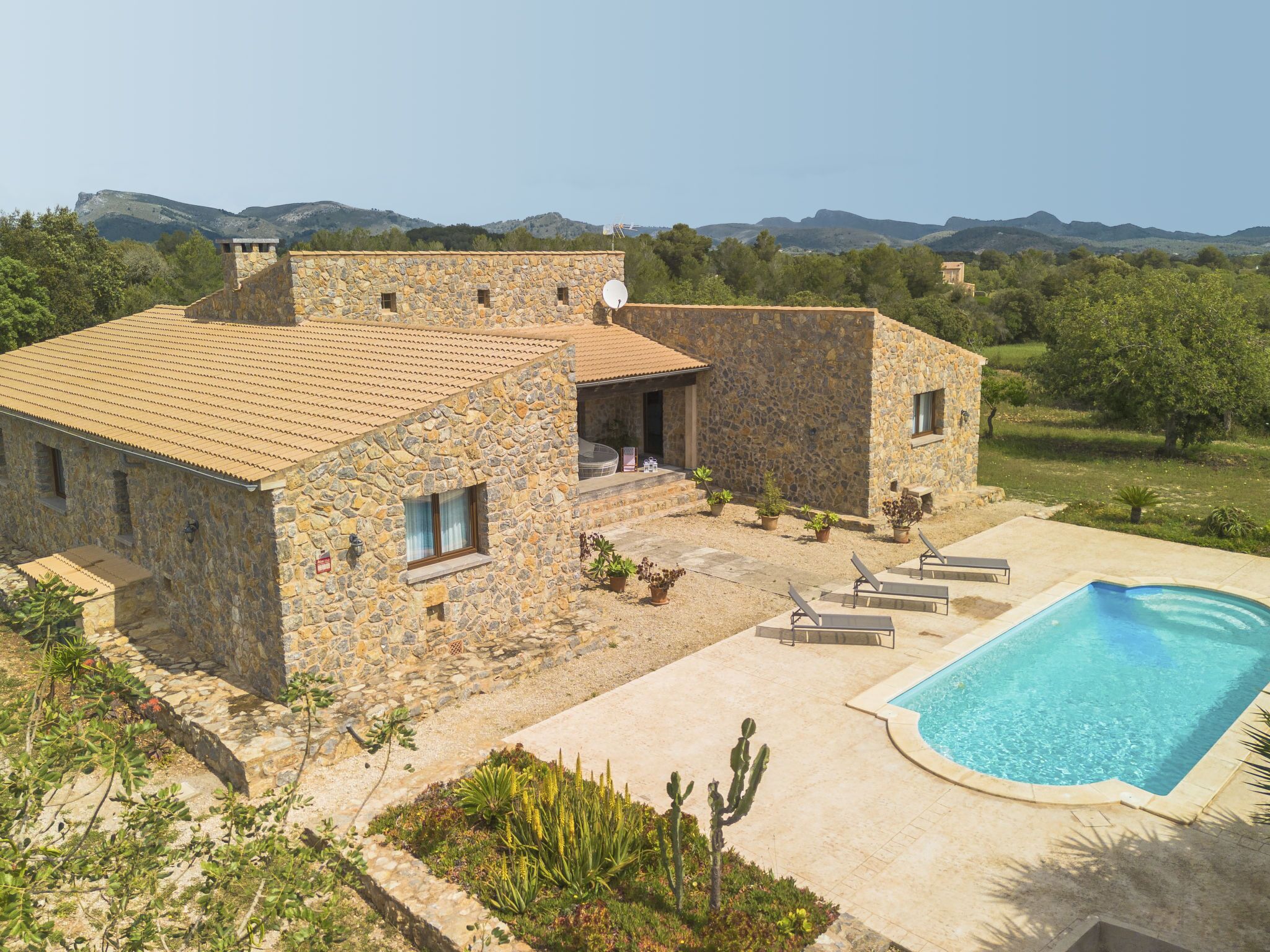 Una villa in pietra con piscina, immersa nel verde e circondata da colline.