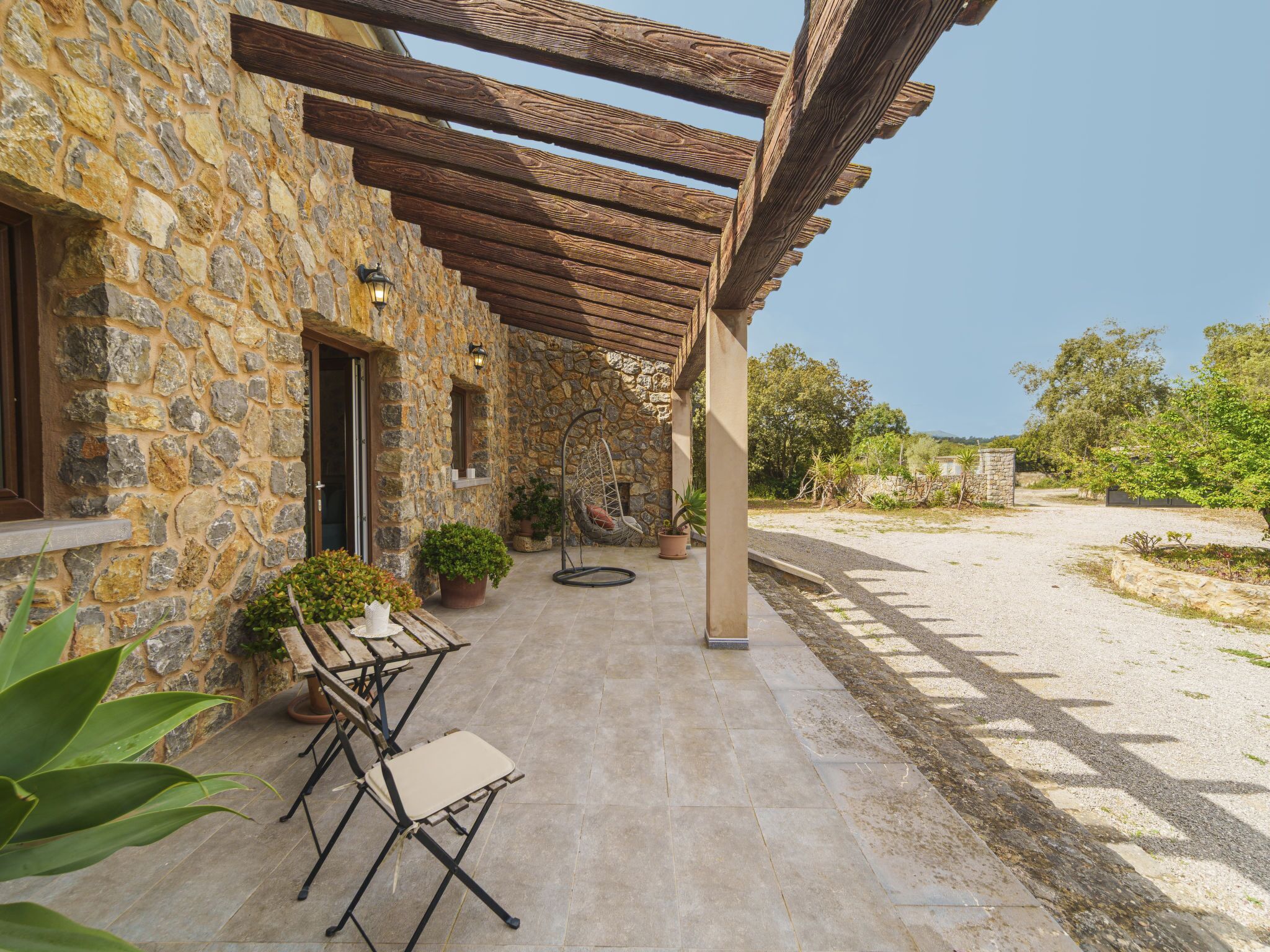 Ein Steingebäude mit einer Pergola, Sitzgelegenheiten im Freien und Topfpflanzen.
