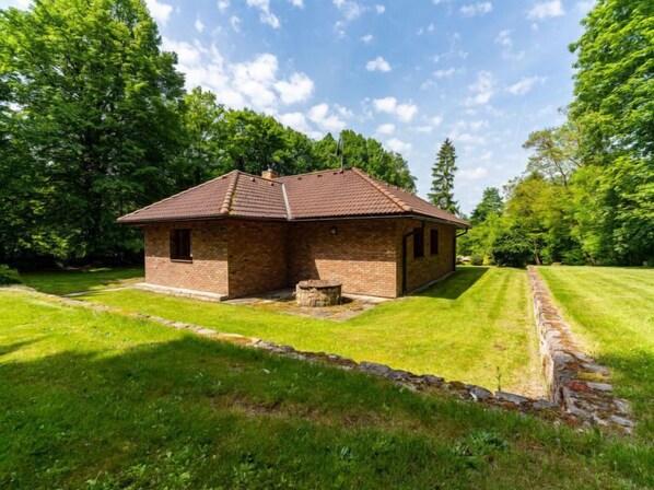 Un petit bâtiment en briques, surmonté d’un toit en tuiles, entouré de pelouses et d’arbres bien entretenus.