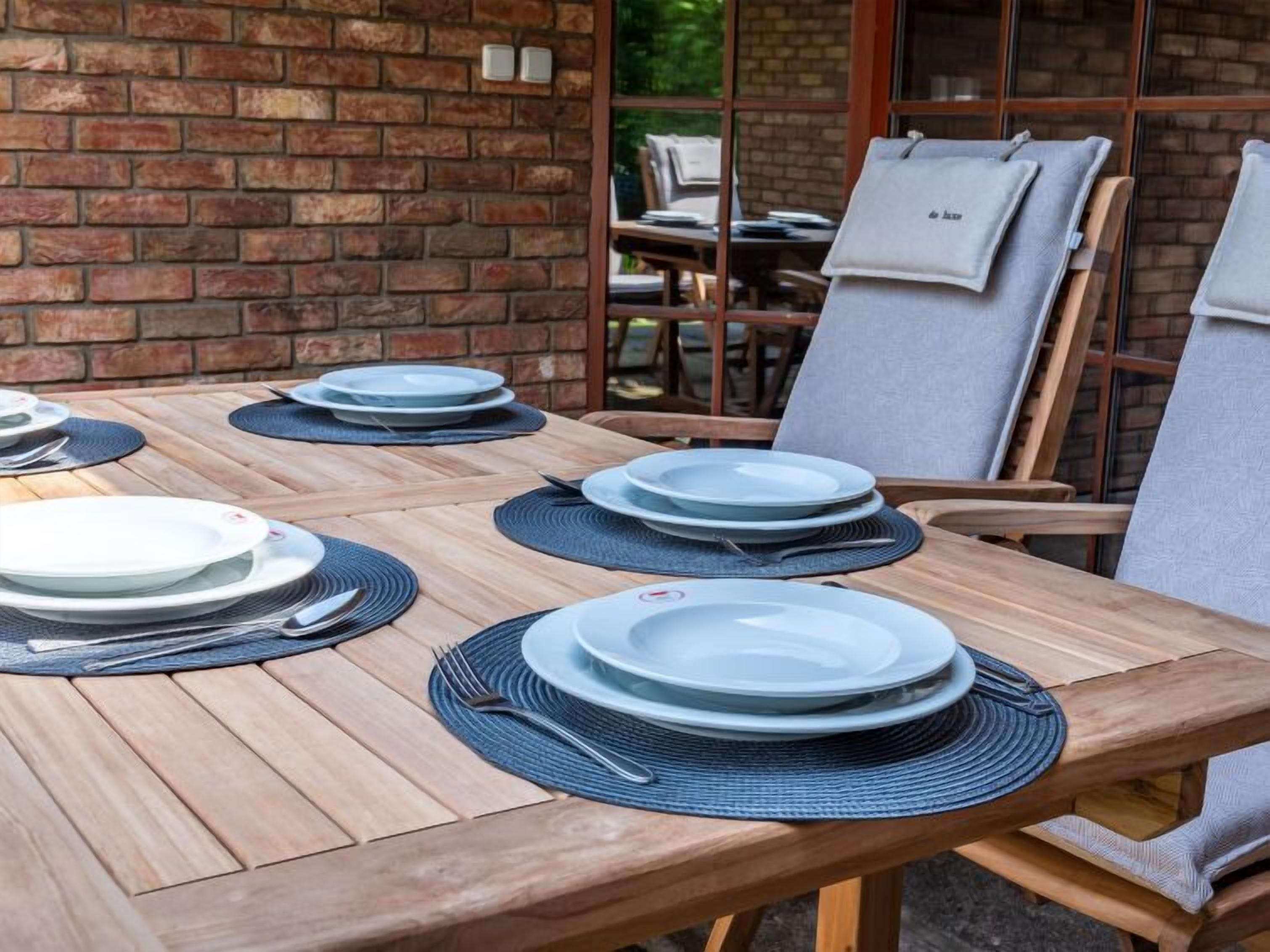 Una mesa de madera con platos y cubiertos, una pared de ladrillo y una ventana al fondo.