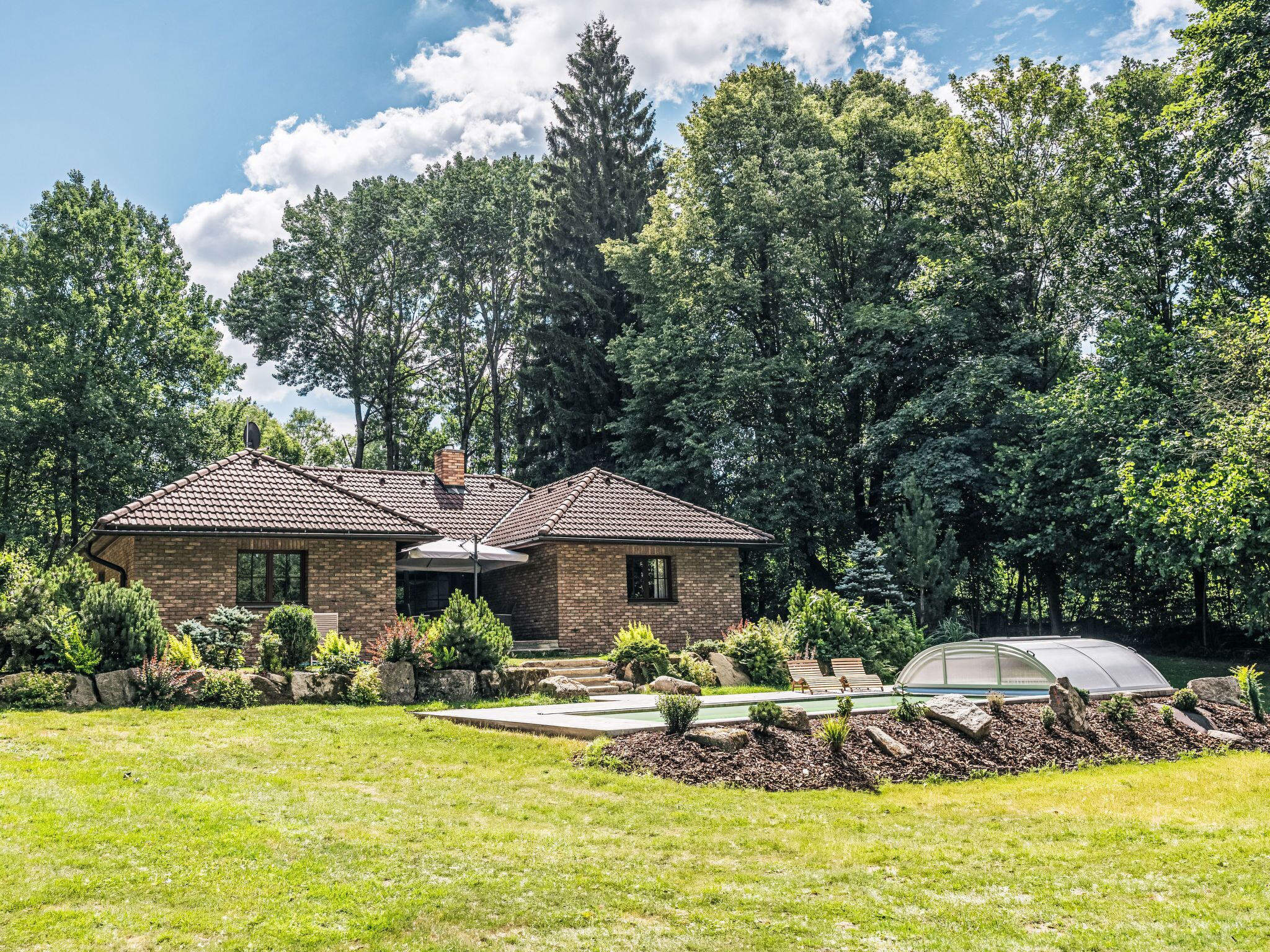 A two-story house with a brick exterior, a tiled roof, and a well-maintained garden with various plants and a greenhouse.