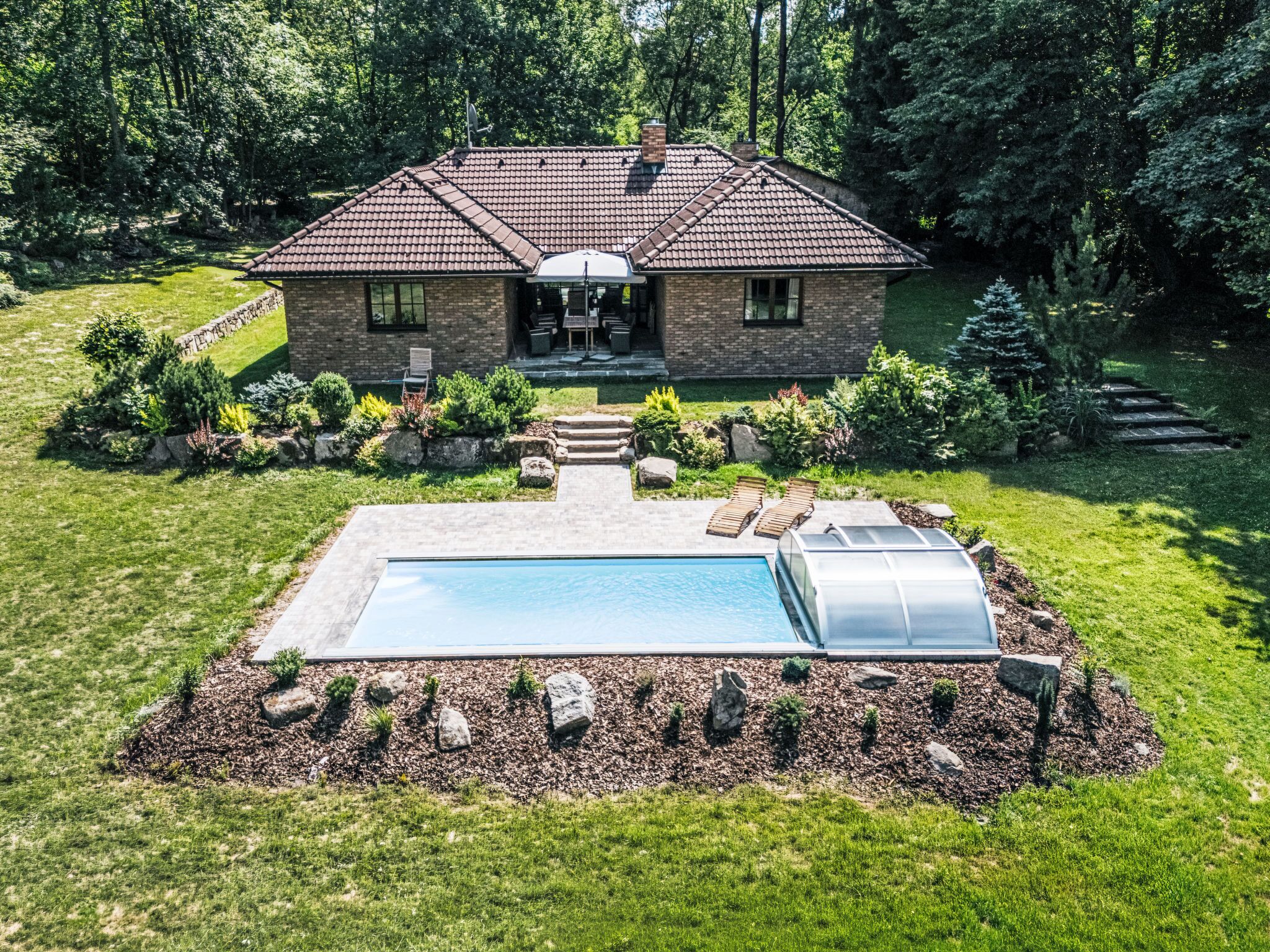 Una casa a due piani con piscina, serra e un giardino curato.