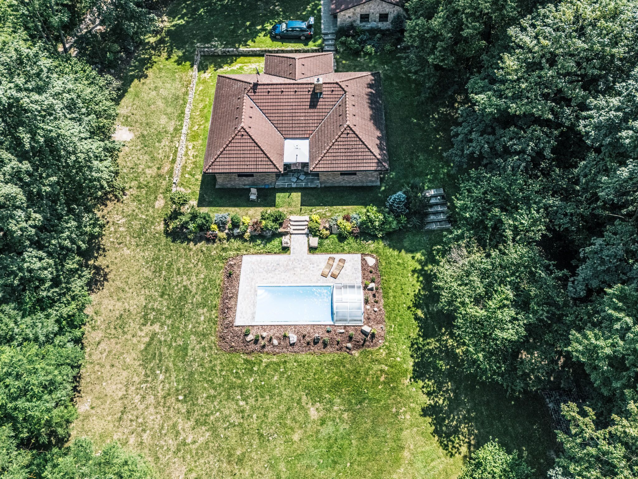 Une vue aérienne d’une maison avec un grand toit, une piscine et une pelouse bien entretenue.