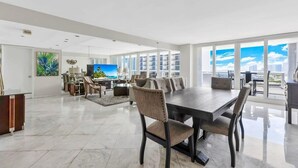 A spacious living area with a large dining table, comfortable seating, and a city view through large windows. - Classic Waterfront Apt | Bay Views | StayCozy (Miami)