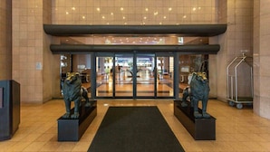 A hotel entrance with a glass door, two lion statues, a tiled floor, and a metal cart. - Bayfront Condo | Elevated amenities | StayCozy (Miami)