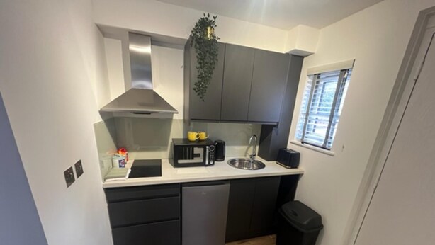 A compact kitchen with dark cabinets, a microwave, a sink, and a small trash bin. - Remarkable Studio Flat in Cambridge (Cambridge)