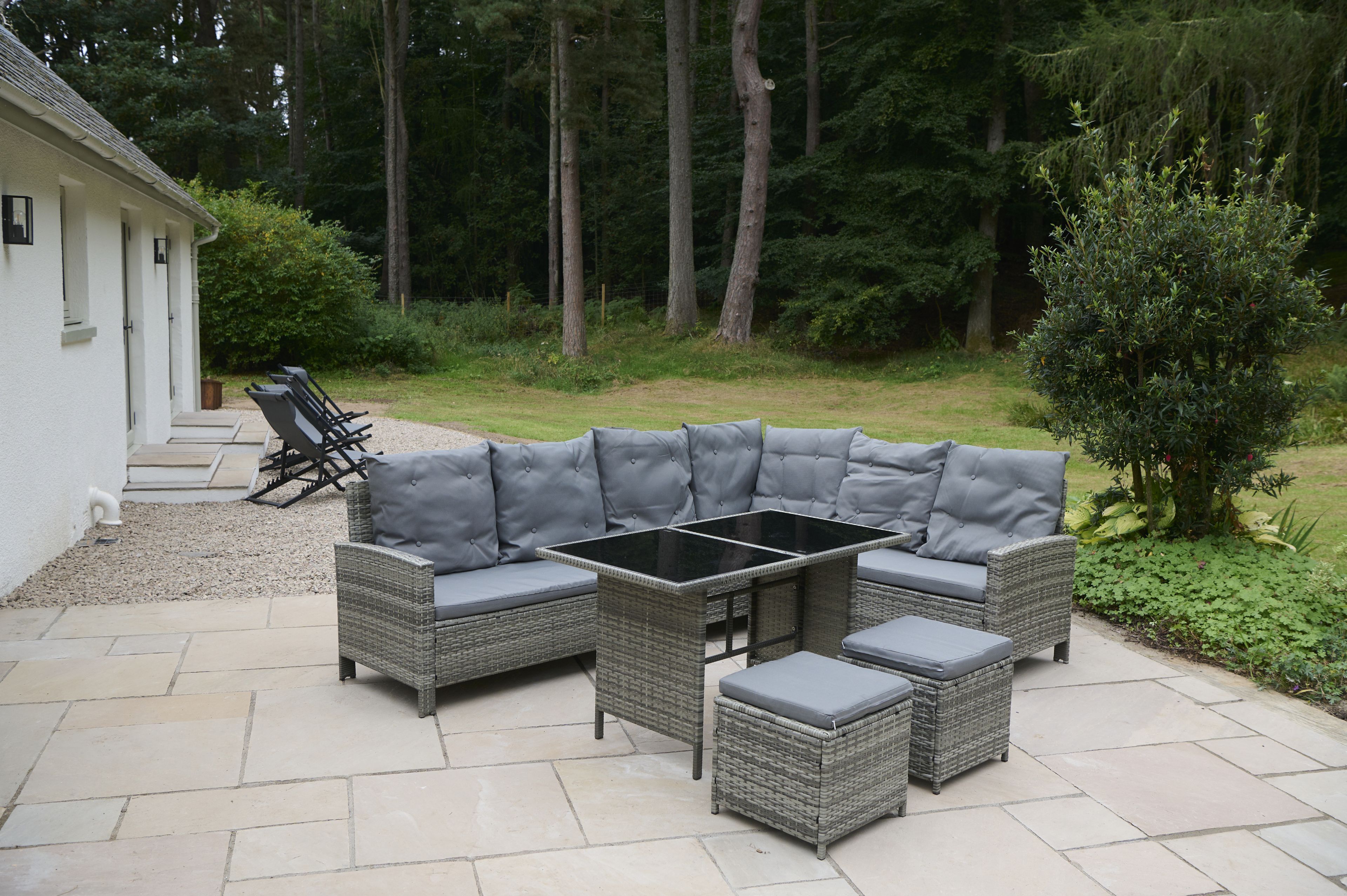 A patio with a gray wicker sectional sofa, a glass-top coffee table, and matching ottomans.