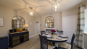 A dining area with a round table, chairs, and a dark-colored buffet with wicker baskets. - Luxury Highland Hideaway with Hot Tub by LochNess (Inverness)