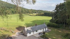 A white cottage with a stone roof, a gravel driveway, and a small garden with a bench. - Luxury Highland Hideaway with Hot Tub by LochNess (Inverness)