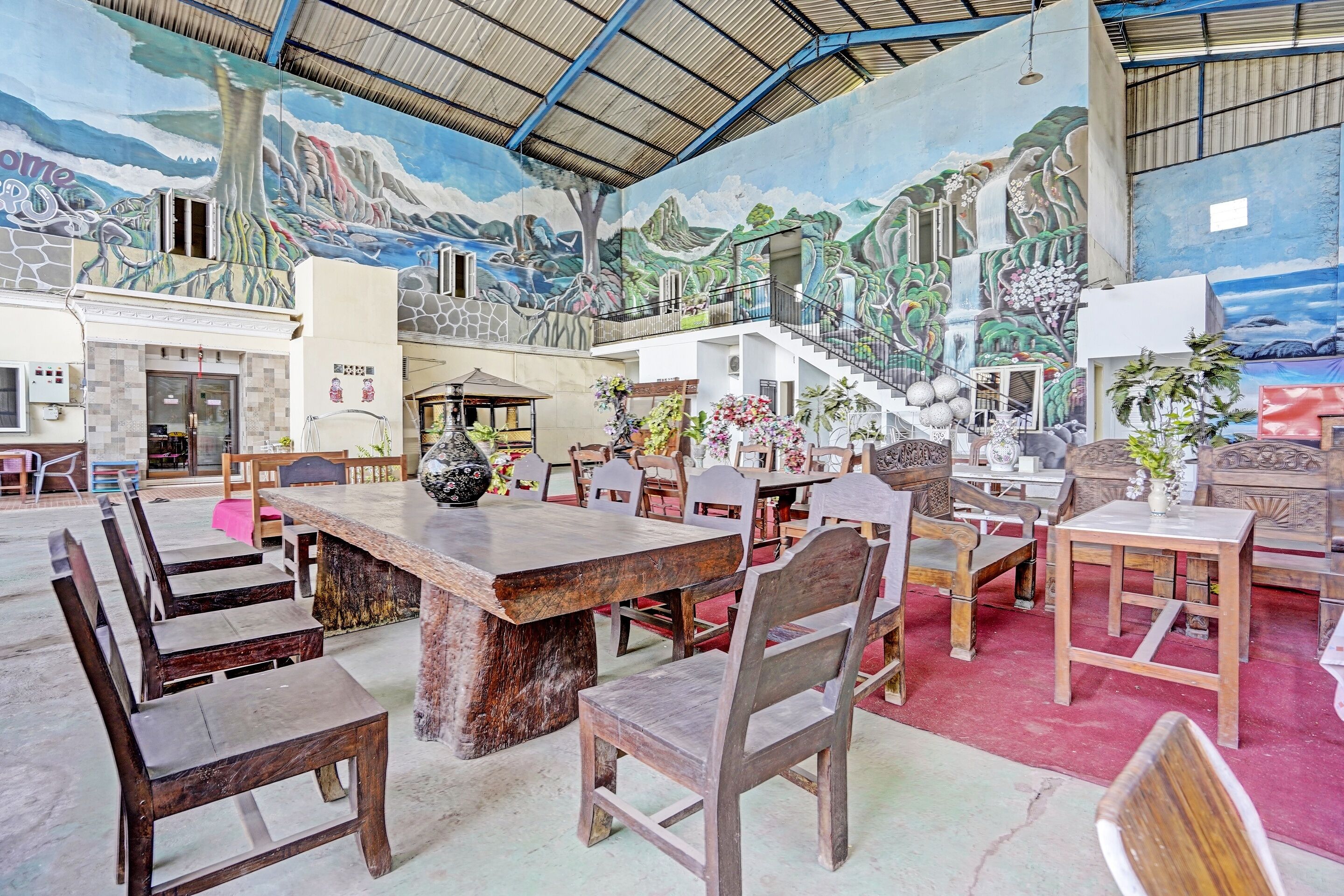 A spacious hall with a high ceiling, a mural depicting a mountainous landscape, and a staircase leading to an upper level.