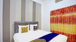 A neatly made bed with a white and blue bedspread, two pillows with geometric patterns, and a colorful floral curtain. - OYO 90943 Mochi 88 Homestay (Jogoroto)