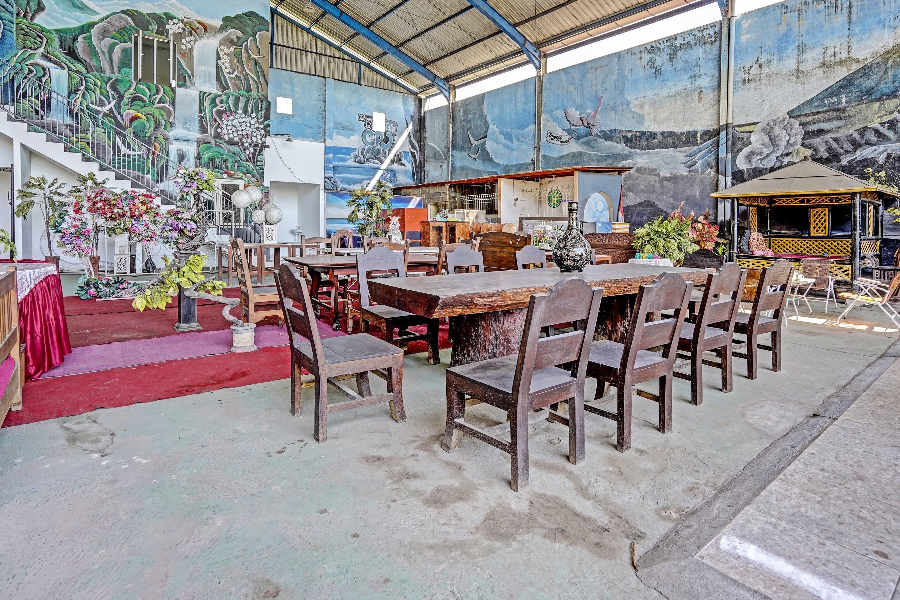 Un comedor con una larga mesa de madera y sillas, rodeado de murales y plantas en macetas.
