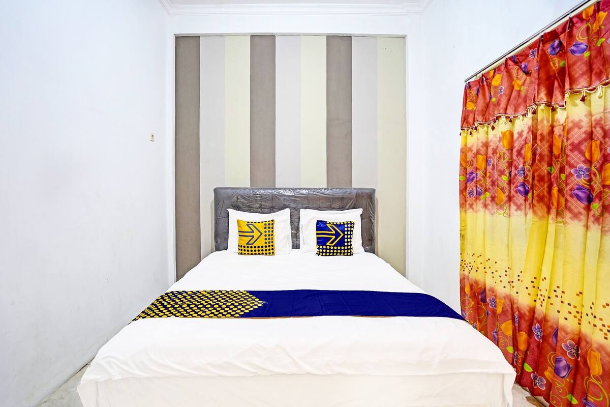 A bed with a striped headboard, two pillows with geometric patterns, and a colorful curtain.