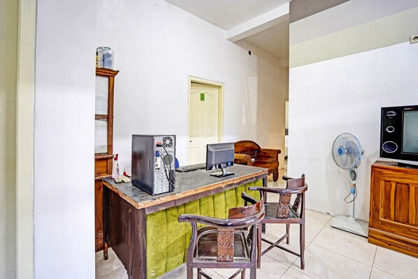 A small kitchen with a wooden counter, two chairs, a computer, and a fan.