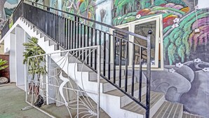 A staircase with a metal railing, a white wall, and a mural with floral and abstract designs. - OYO 90943 Mochi 88 Homestay (Jogoroto)