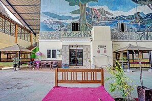 Un patio con un mural, un banco de madera y mesas al aire libre.