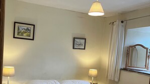 En snyggt bäddad säng med vita sängkläder, två sänglampor, en inramad tavla på väggen och ett fönster med gardiner.