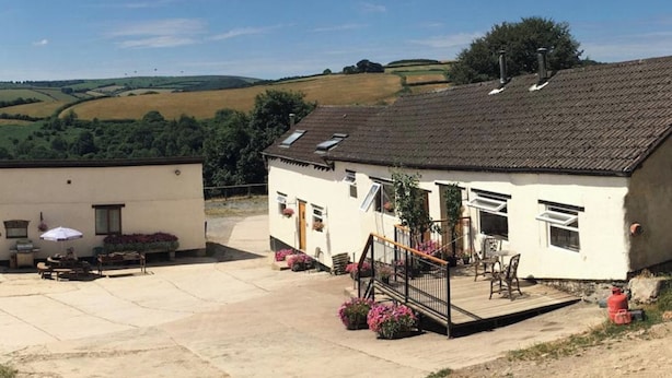 A two-story building with a patio area, outdoor seating, and a view of rolling hills in the background. - Cottage on Exmoor - Sleeps 8 & Parking (Minehead)