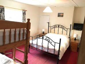 Ein Schlafzimmer mit einem hölzernen Bettgestell, einem Metall-Kopfstück, einem Nachttisch mit Lampe, einem an der Wand befestigten Fernseher und einer Tür.