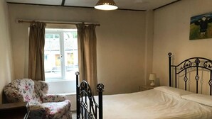Un dormitorio con cama, una silla, una ventana con cortinas y un cuadro en la pared.