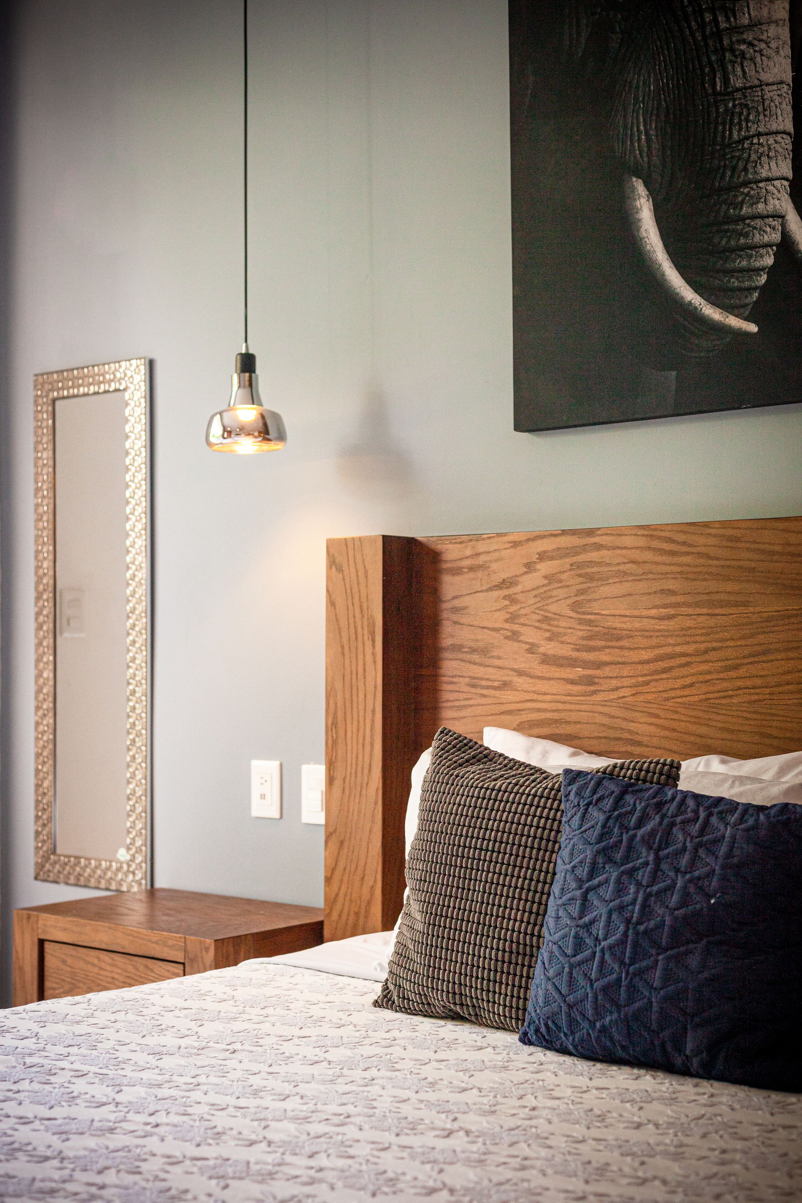 A bedroom with a wooden headboard, a large mirror, and a hanging light fixture.