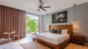 Une chambre moderne avec un grand lit, un ventilateur de plafond, un coin repas avec une table et des chaises, et une vue sur l’extérieur.
