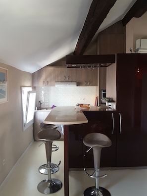 Uma cozinha moderna com armários de madeira escura, bancada branca e dois bancos altos.