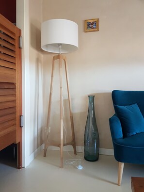 Um quarto com um abajur de madeira, um sofá azul e um vaso.