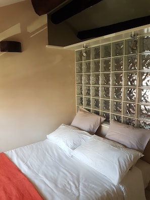 Quarto com cabeceira em bloco de vidro, roupa de cama branca e manta vermelha.