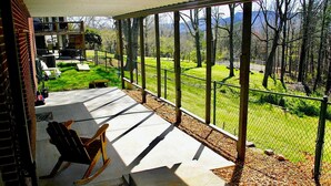 Eine überdachte Terrasse mit einem Schaukelstuhl, Blick auf eine Rasenfläche und einen umzäunten Bereich.