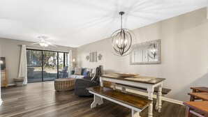 Un vaste salon doté d’une grande porte-fenêtre coulissante donnant sur un patio, d’un coin repas avec un banc en bois et d’un ventilateur de plafond.