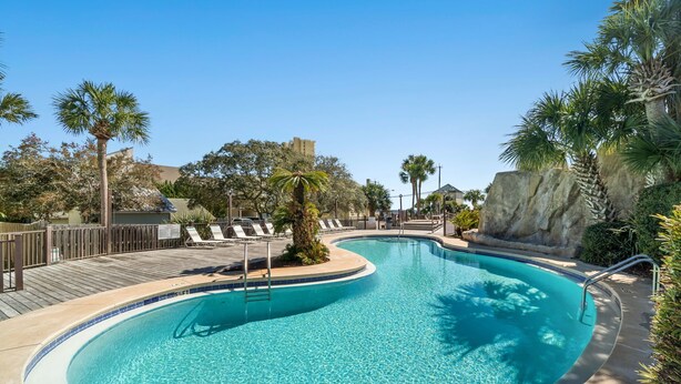 Une piscine d’un bleu éclatant, avec une terrasse en bois, des chaises longues et des palmiers.