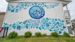 A building with a mosaic mural of blue glass pieces and a circular design, labeled "Ocean Glass Inn". - Ocean Glass Inn - Family Cottage (Rehoboth Beach)